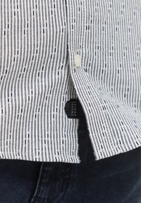 Camicia a righe bianca e blu navy, con linee verticali, una finitura texture e un'etichetta con "FRIDAY CASUAL" vicino all'orlo.