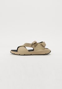 Beige open-toed sandals with adjustable straps, cushioned sole, and textured accents. Lightweight design with black rubber outsole.