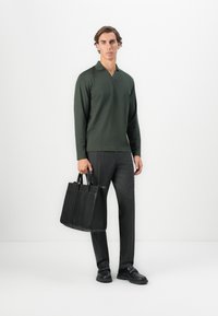 Mørkegrøn langærmet polo skjorte, sorte vertikalt stribede bukser og en sort læder tote bag med fire rum, båret med sorte sko.