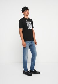 Black t-shirt with a graphic print framed in white, paired with light blue jeans and black footwear featuring a chunky sole.