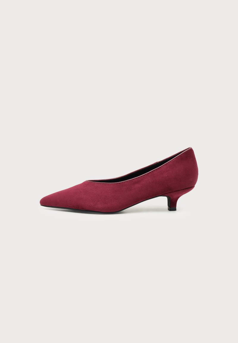 Chaussure à talon kitten en daim bordeaux à bout pointu, avec un talon bas et fin sur fond clair uni.