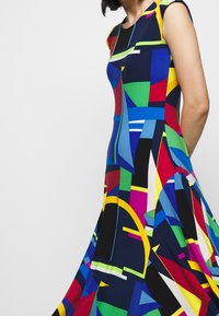 Fitted dress featuring a vibrant abstract pattern in blue, green, red, yellow, and black. Cap sleeves and a flared hemline.