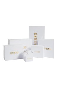 Scatole di imballaggio bianche di varie dimensioni con il logo dorato "GUESS", presentando forme rettangolari e quadrate, alcune con intricati design di piegatura.