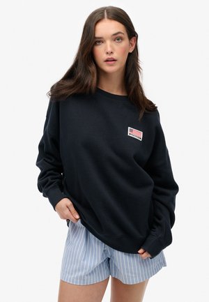 Navy blue sweatshirt made of cotton, featuring a small patch with an American flag design on the chest. Wide crew neckline and long sleeves.