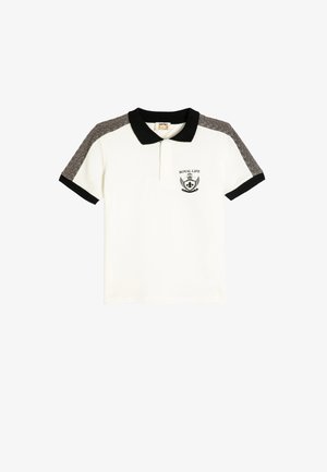 Camiseta polo blanca con collar y mangas negras, que presenta un tejido gris texturizado en los hombros y un emblema en el pecho que dice "ROYAL LIFE".