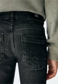 Jeans de mezclilla negra con un diseño ajustado, que presentan dos bolsillos traseros y costuras visibles. La cinturilla muestra la etiqueta "LTB."