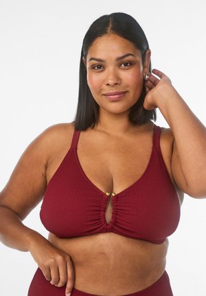 Kvinde med mellemtonet hudfarve og glat sort hår, iført en struktureret bordeaux bikini top med guldknapdetalje på hvid baggrund.