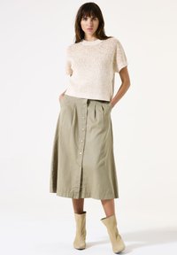 Crème gebreide trui met korte mouwen, gecombineerd met een khaki midi rok met een voorknoopsluiting en plooien, gedragen met beige enkelhoge laarzen.