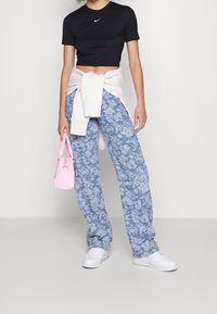 Svart kortärmad Nike-t-shirt, blå blommönstrade byxor, ljusrosa tröja knuten i midjan, rosa handväska och vita sneakers.