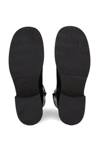 Sole nere di scarpe con una texture liscia e il logo in rilievo "Calvin Klein Jeans". Progettate con hardware minimal e forma rettangolare.