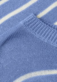 Tissu tricoté bleu clair avec un poignet côtelé plié posé sur un fond tricoté rayé bleu et blanc.
