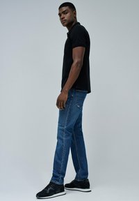 Camisa polo de manga corta negra combinada con jeans de mezclilla azules y zapatillas deportivas negras, mostrando un diseño ajustado y un estilo casual.