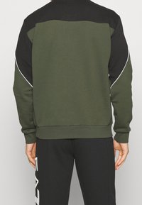 Olivgrön sweatshirt med svarta axlar, vit kantning, långärmade och ribbad nederkant. Kombinerad med svarta byxor med vit grafisk text.