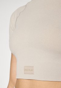 Bežani rebrasti crop top s kratkim rukavima i prilagođenim dizajnom. Ima mali natpis "ONLY PLAY" na prednjem rubu. Glatka tekstura.