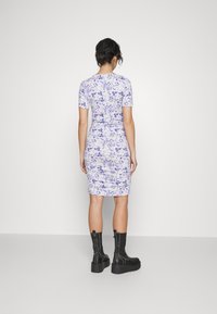 Sukienka krótka z krótkim rękawem w kwiatowy wzór w odcieniach lawendy i niebieskiego; dopasowana sylwetka z marszczeniami; noszona z czarnymi, platformowymi botkami za kostkę.