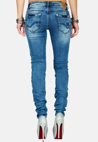 Jeans in denim blu slim con una finitura sbiadita, dotati di tasche posteriori con design a chevron e un'etichetta in pelle marchiata. Abbinati a tacchi alti argentati.