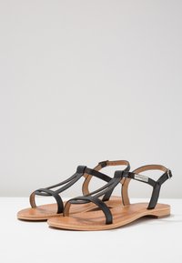 Sandali neri in pelle con più cinturini, suola piatta e soletta in pelle marrone. Cinturino alla caviglia regolabile con dettagli in metallo argentato.