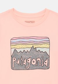 Hellrosa Baumwoll-T-Shirt mit einem grafischen Design von Bergen, geschichteten Farben und dem Wort "Patagonia" in fetter Schrift.