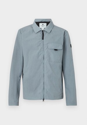 Chaqueta de manga larga azul clara con cuello, cierre frontal y un bolsillo en el pecho. Presenta un acento negro en el brazo izquierdo. Textura suave.