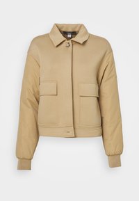 Beżowa krótka kurtka z kołnierzem, zamykana na guziki z przodu, z dwiema dużymi kieszeniami naszytymi oraz teksturowanymi rękawami. Miękki materiał z elastycznymi mankietami.