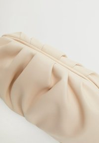 Sac à main beige avec un design froncé, fabriqué en matériau lisse. Il dispose d'une fermeture éclair sur le dessus et d'une surface douce et texturée.