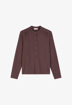 Haut à manches longues en mauve profond, avec un col henley à boutons et des détails froncés aux épaules. Tissu doux avec un minimum de marquage.