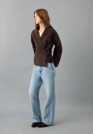 Chaqueta marrón acolchada con cierre de lazo, combinada con jeans de mezclilla azul claro de talle alto y corte recto. Zapatos negros completan el conjunto.