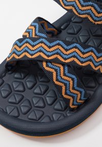 Černé gumové sandály se zigzagovými popruhy v modré a oranžové barvě. Texturovaná podrážka má diamondové tvary pro lepší přilnavost.