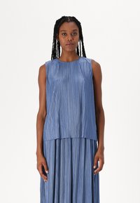 Rochie albastră, fără mâneci, cu pliuri verticale. Textură netedă, decolteu rotund, design în straturi. Se oprește la jumătatea gambei, cu un finisaj subtil, strălucitor.