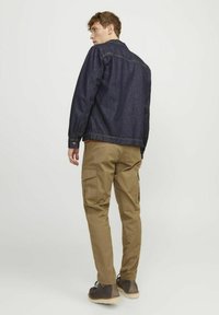 Donker denim jack met zichtbare stiksels, gecombineerd met khaki cargobroek met grote zijzakken, gedragen met bruin veterschoen.