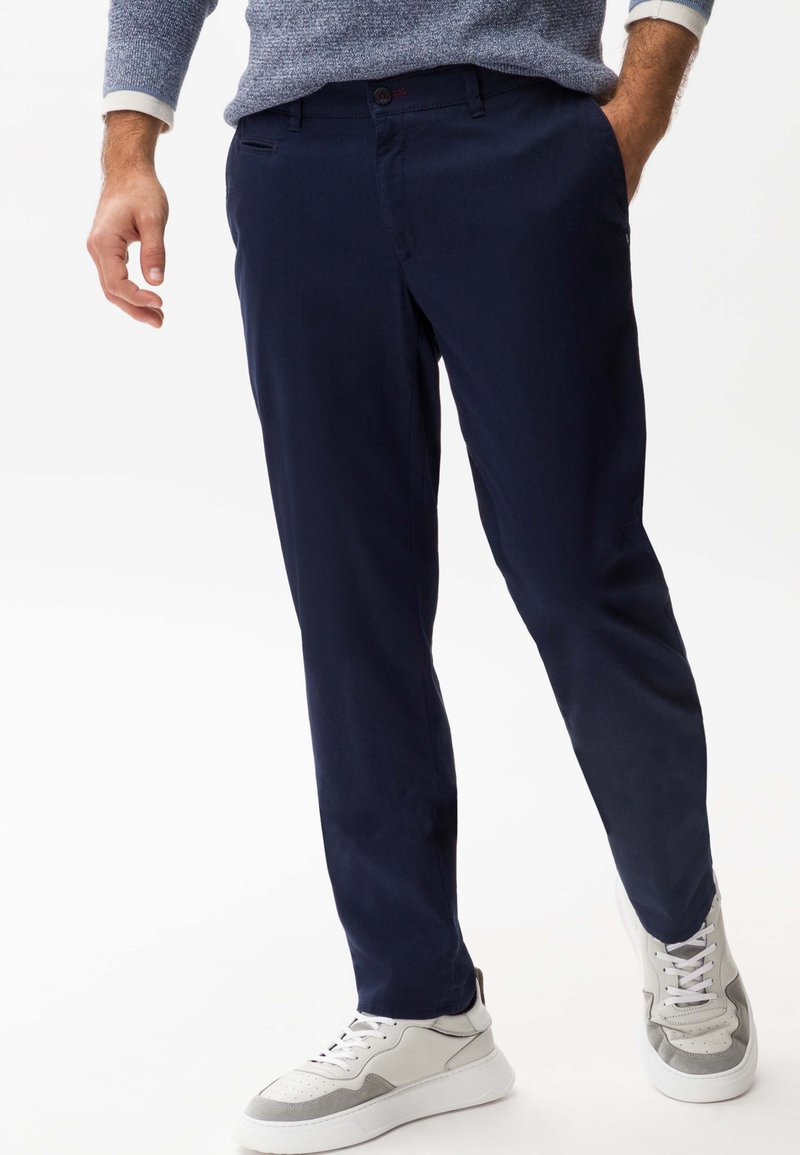 Pantalon marine en tissu lisse, avec une coupe slim et une taille plate. Associé à des baskets gris clair et blanches.