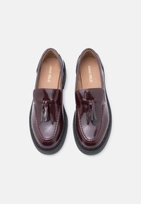 Μοκασίνια από βουργουνδίας δερμάτινο πατέντα με λεπτομέρειες φούντας, στρογγυλή μύτη και μαύρη λαστιχένια σόλα. Διαθέτουν ραμμένες διακοσμήσεις κατά μήκος της άκρης.