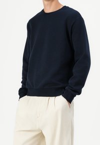 Marineblå sweatshirt i bomullsblandning, rund halsringning, ribbade muddar och fåll, avslappnad passform, kombinerad med beige byxor. Enkel, enfärgad design.