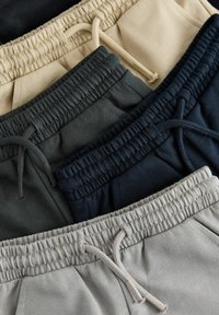 Pile de pantalons de survêtement beige, gris foncé, marine et gris clair avec taille élastique et cordons de serrage en gros plan.
