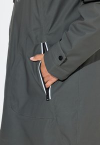 Parka gris con una textura suave, que presenta un bolsillo con cremallera con ribete blanco y un detalle de puños abotonados.