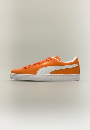 Zapatilla de perfil bajo en ante naranja con raya blanca de Puma y suela de goma blanca mostrada de lado sobre un fondo neutro.