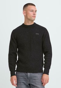 Sort strikket sweater med et tekstureret mønster, rund halsudskæring og båndede ærmer. Har et lille, minimalistisk logo på brystet.