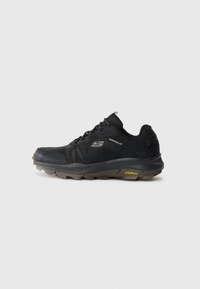 Chaussure de sport noire avec tige synthétique, panneaux texturés et fermeture à lacets. Dotée d'une semelle rembourrée et d'un profil de semelle robuste pour une bonne traction.