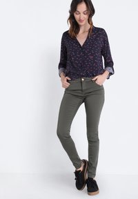 Blusa de manga larga azul marino con estampado floral y puños enrollados, combinada con pantalones ceñidos verde oliva y zapatillas negras con suela marrón.