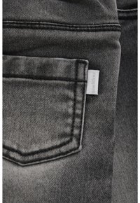 Zbli żenie na wyblakłą czarną kieszeń na dżinsach z czarnymi szwami i białą metką marki po prawej stronie.