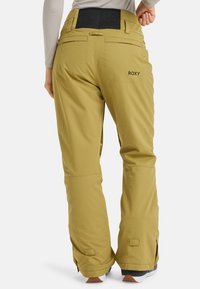 Pantaloni da neve gialli con una cintura elasticizzata nera, aperture laterali con zip e logo Roxy sulla tasca posteriore. Realizzati in materiale morbido e impermeabile.