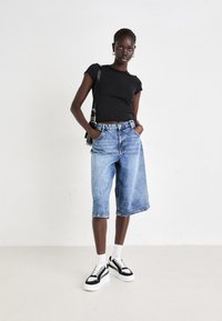 Culottes en denim bleu avec un lavage léger, taille haute, poches latérales, associées à un haut noir à manches courtes et des baskets compensées noires.