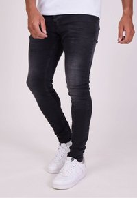 Jeans ajustados de mezclilla negra con una textura desgastada, equipados con un clásico diseño de cinco bolsillos, combinados con zapatillas blancas.