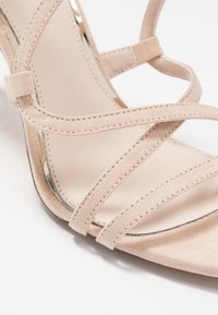 Beige mockask häl sandal med korsade remmar, slät foder och en elegant öppen tå-design med subtila sömdetaljer.