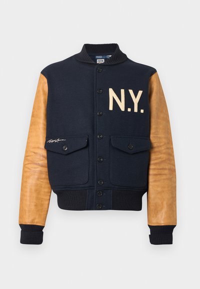 Navy wool blend bomber jacket with brown leather sleeves, features “N.Y.” in cream, ribbed cuffs, and two front pockets.