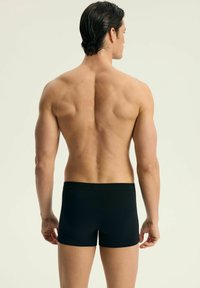 Czarne bokserki, wykonane z gładkiej tkaniny, dopasowany krój, średni stan, z minimalnymi szwami i bez widocznego oznakowania.