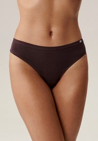 Brązowe figi bikini o gładkiej strukturze, z wysokimi wycięciami na nogi i miękkim pasem. Minimalistyczny design z małą metką marki z boku.