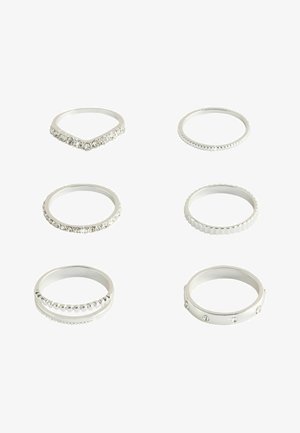 Six silver rings with various designs including smooth bands, textured edges, and embedded clear stones arranged on a white background.