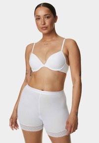 Reggiseno bianco sagomato con spalline regolabili e slip bianchi coordinati con merletto sul bordo. Tessuto liscio con design senza cuciture.