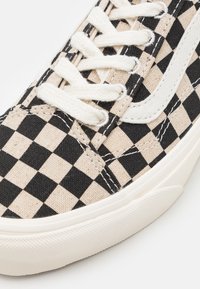 Schwarz-beige karierter Segeltuch-Sneaker mit weißen Schnürsenkeln und Seitenstreifen, ausgestattet mit einer Gummisohle und strukturiertem Material.